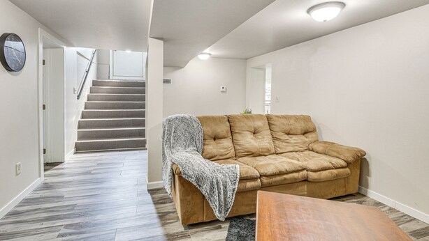 A living room with a brown sofa, a wooden coffee table, and a staircase leading to another room. - Cozy Sturgis Retreat - Walk to Main St & Saloons! (Sturgis)