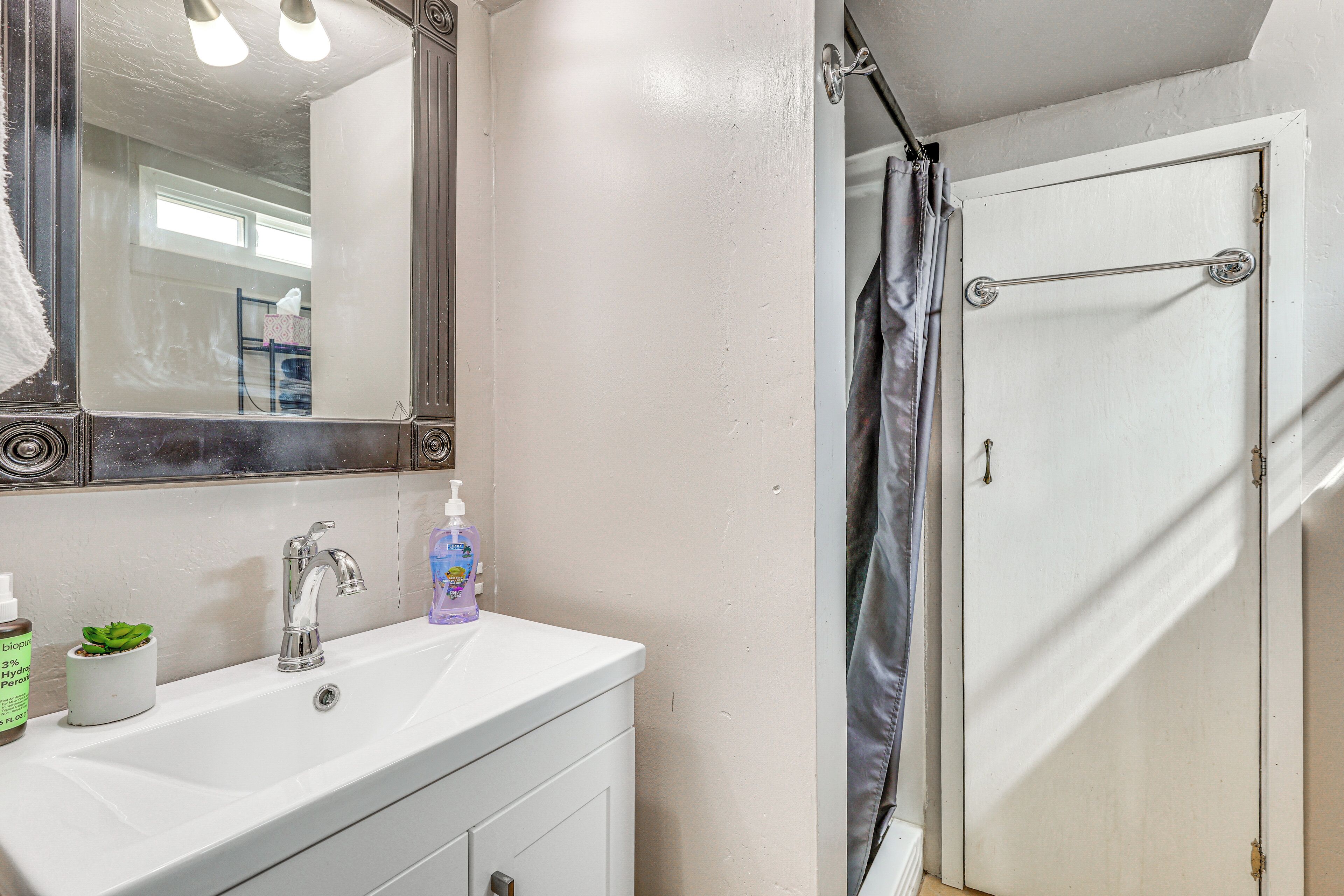 Un baño con un lavamanos blanco, un espejo y una cortina de ducha.
