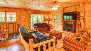 A wooden cabin interior with a fireplace, a ceiling fan, and a large window. - Riverfront Rutherfordton Retreat w/ Fire Pit! (Rutherfordton)