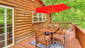 A wooden cabin with a deck, a dining table with chairs, and a red umbrella. - Riverfront Rutherfordton Retreat w/ Fire Pit! (Rutherfordton)