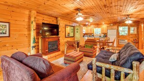 A log cabin interior with a fireplace, wooden furniture, and a kitchen area. - Riverfront Rutherfordton Retreat w/ Fire Pit! (Rutherfordton)