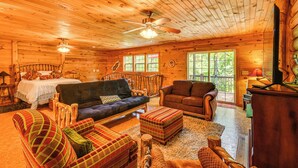 A cozy cabin interior with wooden walls, a bed, a sofa, a chair, and a television. - Riverfront Rutherfordton Retreat w/ Fire Pit! (Rutherfordton)