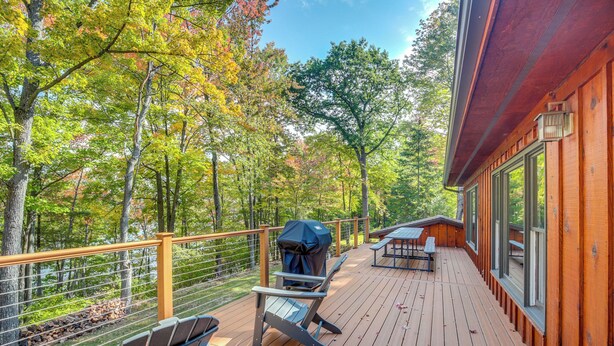 A wooden deck with outdoor seating, a grill, and a view of a forested area. - Rhinelander Chain of Lakes Home w/ River Dock! (Rhinelander)