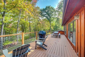 A wooden deck with outdoor seating, a grill, and a view of a forested area. - Rhinelander Chain of Lakes Home w/ River Dock! (Rhinelander)
