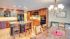 A modern kitchen with wooden cabinets, a central island, and a dining table with chairs. - Rhinelander Chain of Lakes Home w/ River Dock! (Rhinelander)