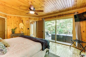 A wooden-paneled bedroom with a bed, a ceiling fan, a large window, and a view of the outdoors. - Creekside Cabin Rental ~ 8 Mi to Downtown Ellijay! (Ellijay)