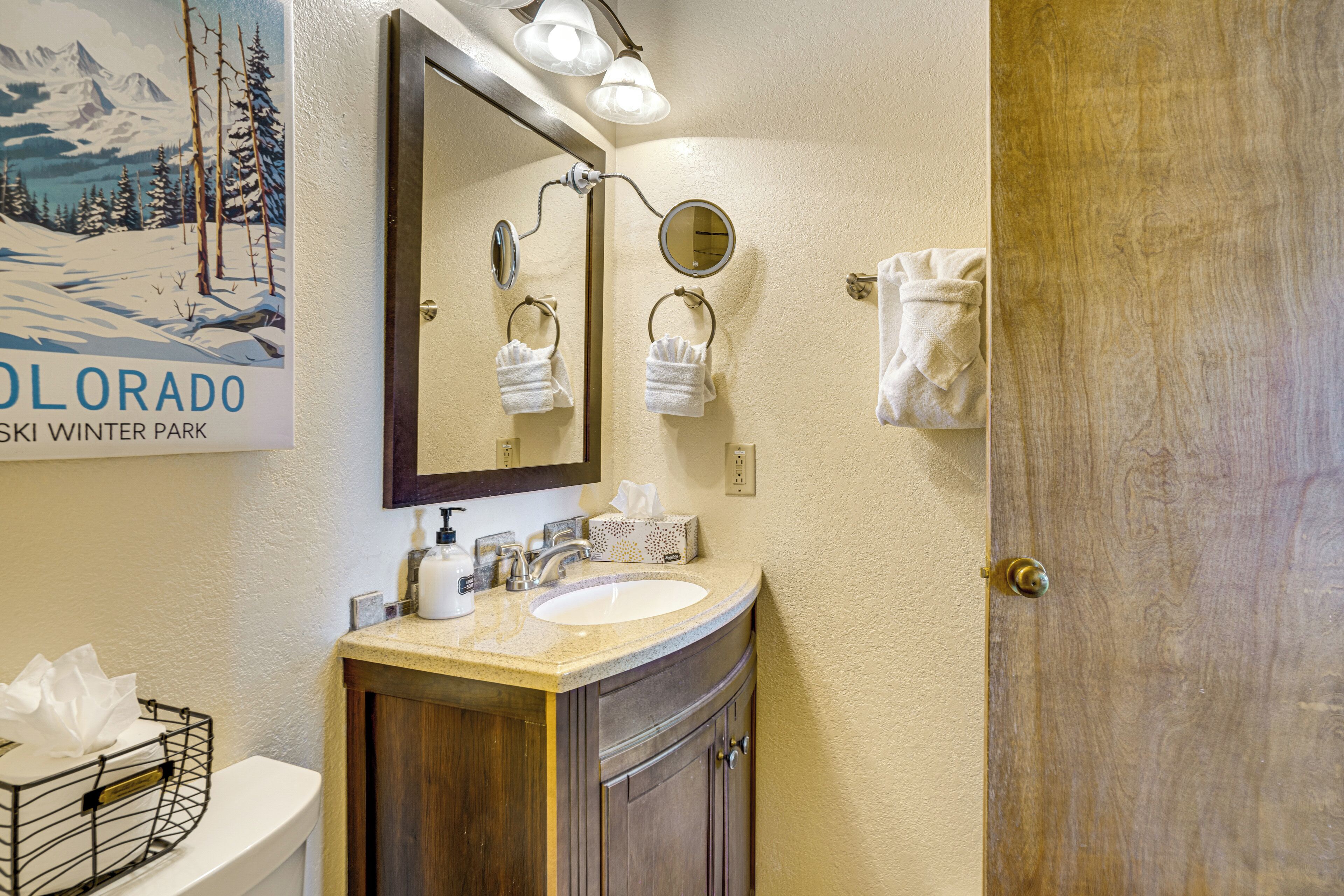 Een badkamer met een wastafel, spiegel, handdoekrek en een poster van Colorado Winter Park.