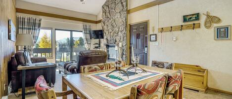A dining area with a wooden table, chairs, a ceiling fan, and a stone wall.