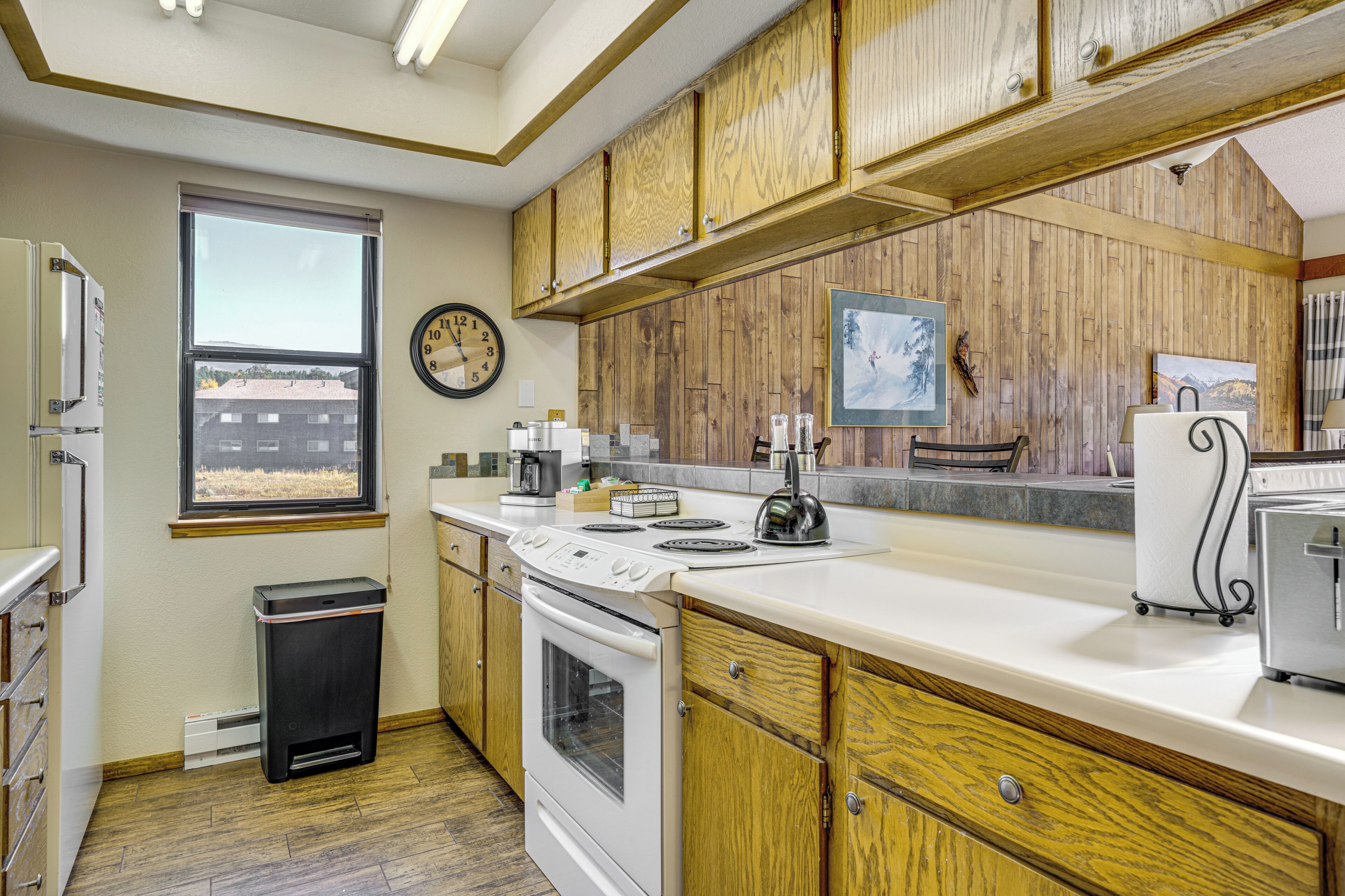 A kitchen with wooden cabinets, a stove, a sink, and a window with a view.