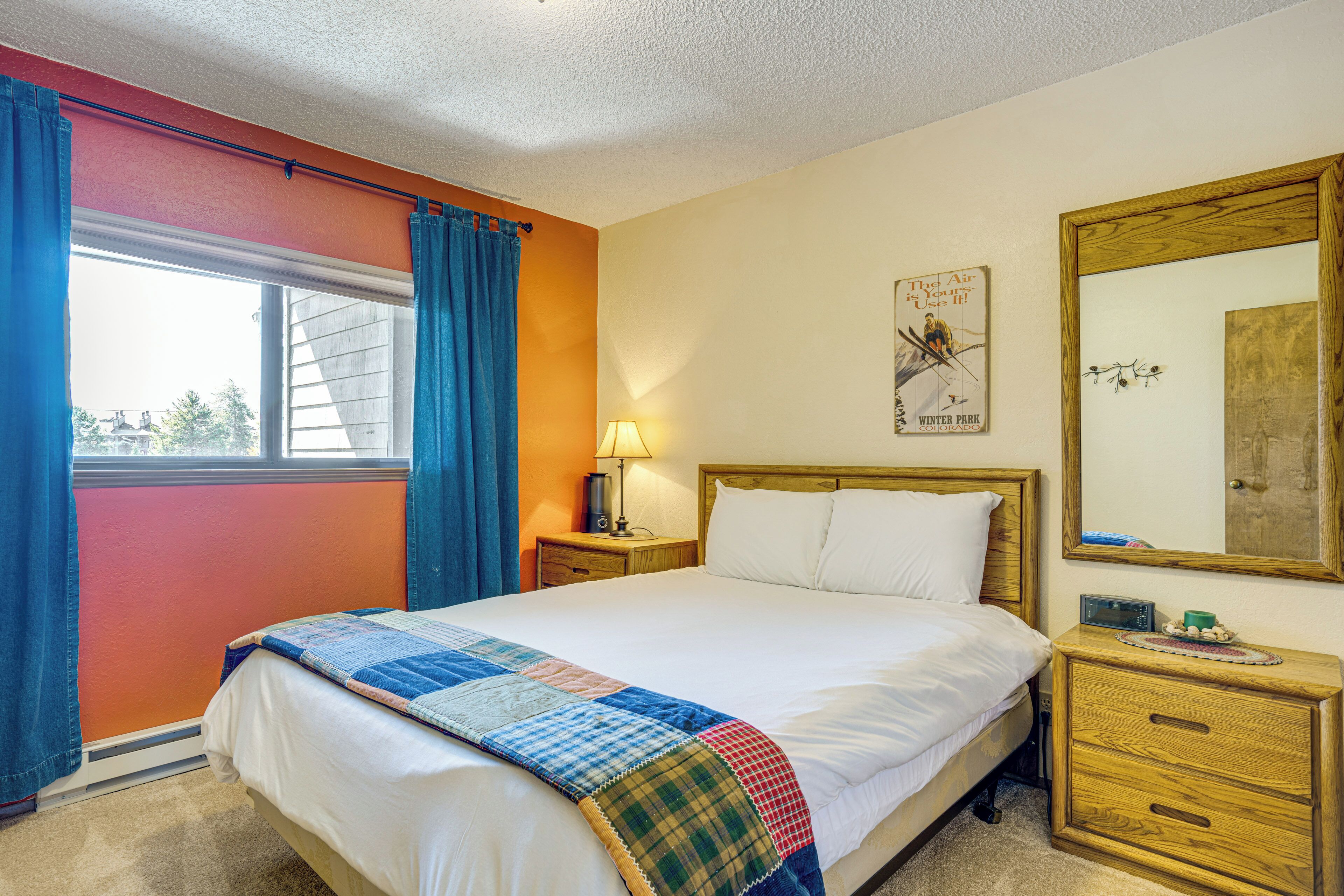 A bedroom with a bed, a nightstand, a lamp, a mirror, and a window with curtains.