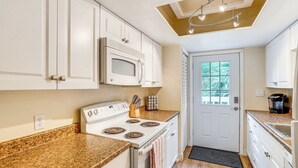 A kitchen with white cabinets, a white stove, granite countertops, and a window with a view of greenery. - Half-mi to Riverwalk: Charming Sanford Retreat! (Sanford)