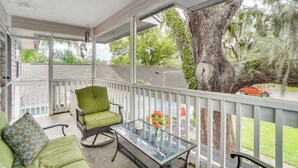 A covered porch with a glass table and a green chair, overlooking a tree and a street. - Half-mi to Riverwalk: Charming Sanford Retreat! (Sanford)