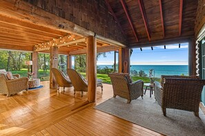 A wooden deck with wicker furniture, large windows, and a view of the ocean.