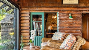 Interior acogedor de una cabaña de madera con un sofá de mimbre, una puerta verde y una chimenea de piedra.
