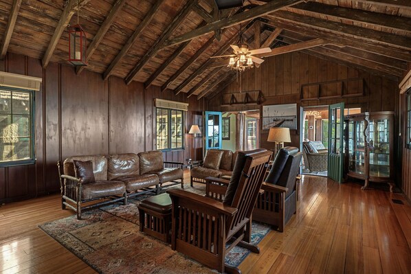 A spacious living room with wooden floors, leather sofas, and a large chandelier.