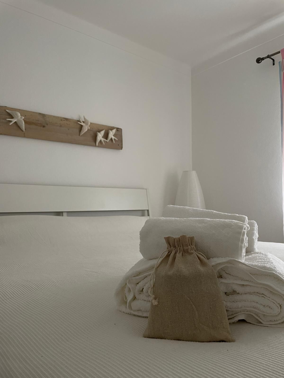 A neatly made bed with folded towels and a small bag on a textured white bedspread.