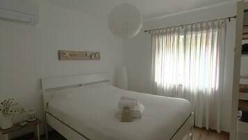 Ein Schlafzimmer mit einem Einzelbett, einem Nachttisch mit Lampe, einer Wand-Klimaanlage und einem Fenster mit Vorhängen.