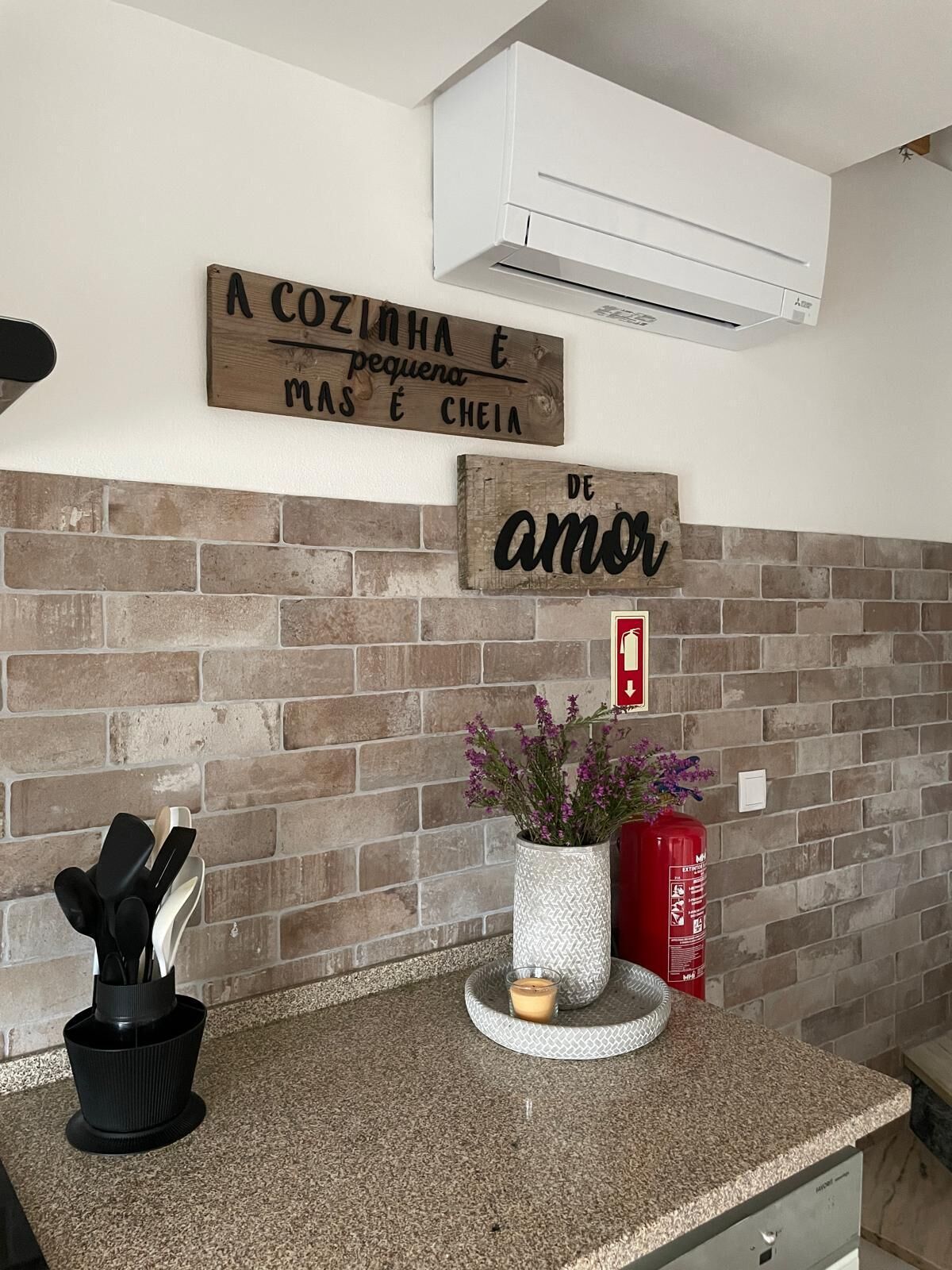 A kitchen with a brick backsplash, a wooden sign above the sink, a potted plant, a candle, and a fire extinguisher.