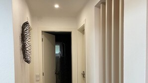 A hallway with a wooden floor, white walls, and a staircase with a wooden handrail.