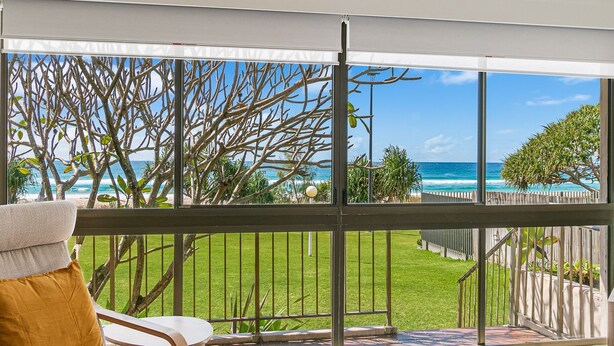 A balcony with a view of the ocean, a grassy area, and a wooden fence.