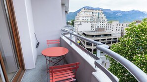 A balcony with a red table and chairs, overlooking a cityscape and mountains. - Le Cashmere - au centre de tout (Annecy)
