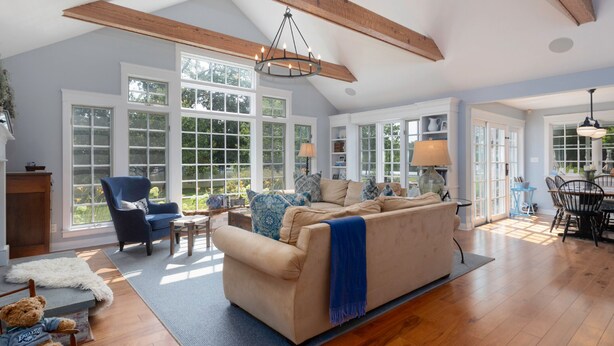 A spacious living room with a large beige sofa, a blue armchair, and a wooden dining table. - Minutes from Downtown St. Michaels | Pool | Outdoor Kitchen | Private Dock | Hot (Easton)