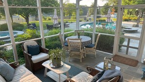 A covered patio with wicker furniture, a checkered table, and a view of a swimming pool. - Minutes from Downtown St. Michaels | Pool | Outdoor Kitchen | Private Dock | Hot (Easton)