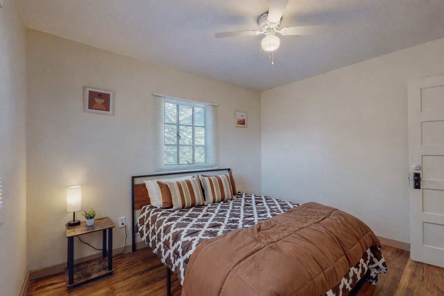 Quarto com cama, mesa de cabeceira, janela e ventilador de teto.