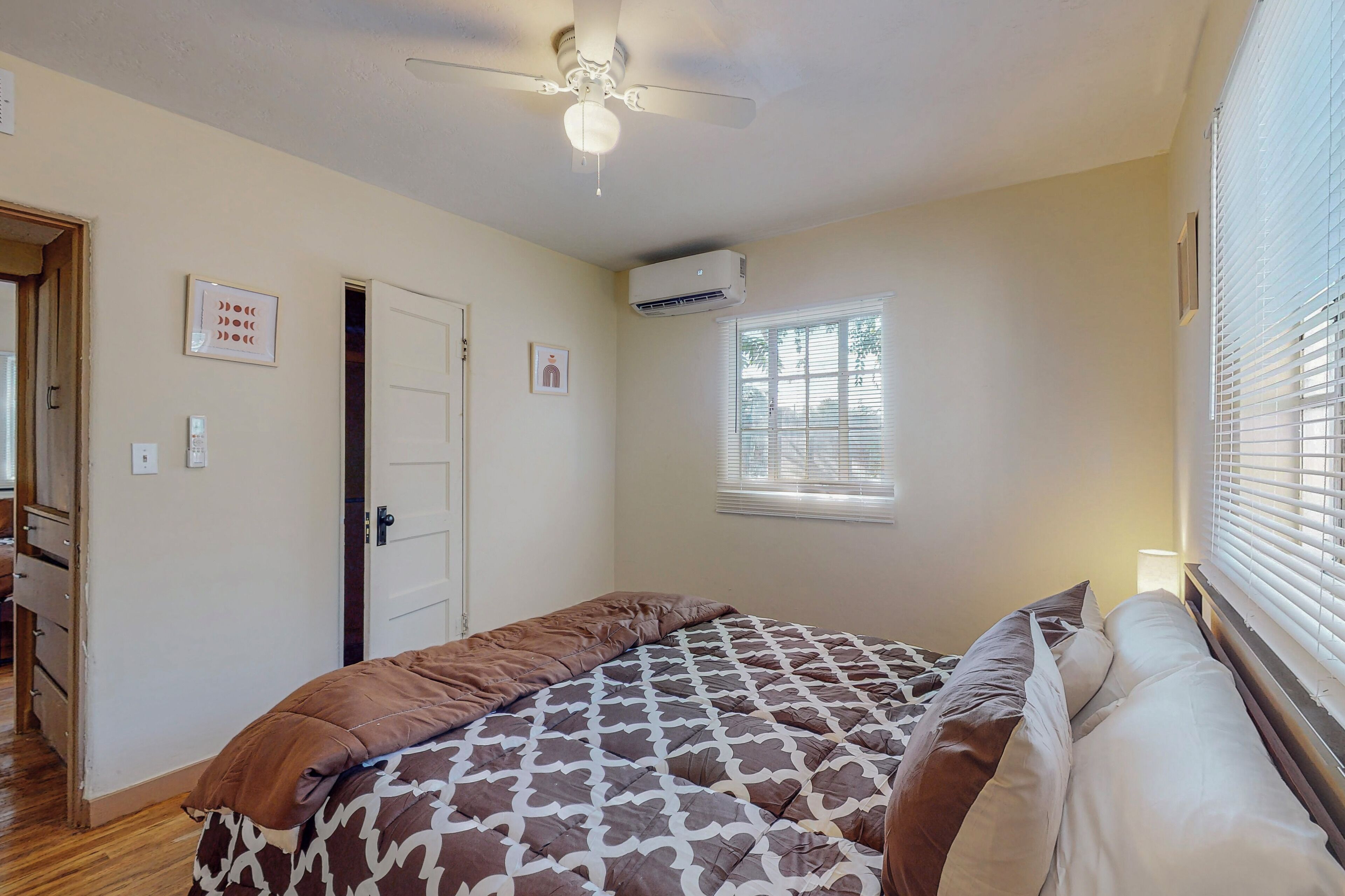 Een slaapkamer met een bed, plafondventilator, airconditioning en een raam met zonwering, plus een deur.