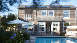 A two-story house with a swimming pool, a balcony, and a covered patio area. - Beachfront House w Pool Steam (Chichester)
