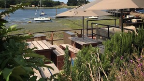 A riverside patio with picnic tables, a covered seating area, and boats in the background. - Idyllic 3 Bed Country Cottage (Chichester)