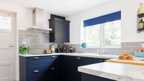 A modern kitchen with dark blue cabinets, a white countertop, and a window with a view of trees. - Idyllic 3 Bed Country Cottage (Chichester)