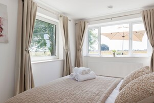 Un dormitorio con cama, cortinas color beige, una ventana y vista a árboles.