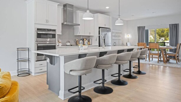 A modern kitchen with white cabinetry, a central island with bar stools, stainless steel appliances, and pendant lighting. - Downtown Wake Forest Luxury Condo | Rooftop Terrace + EV Charger (Wake Forest)