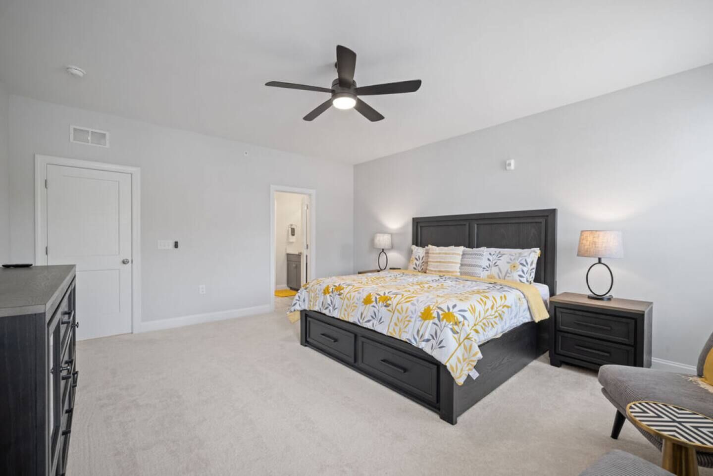A bedroom with a bed, bedside tables, a ceiling fan, and a dresser.