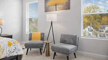 A bedroom with two gray armchairs, a floor lamp, a bed with a yellow blanket, and a painting of a tree.