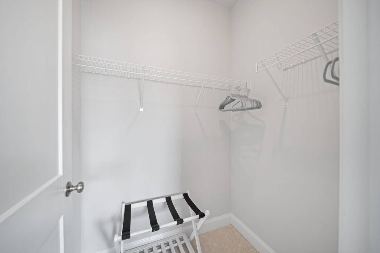 A small, white-walled closet with a metal rack and a hanging shoe rack.