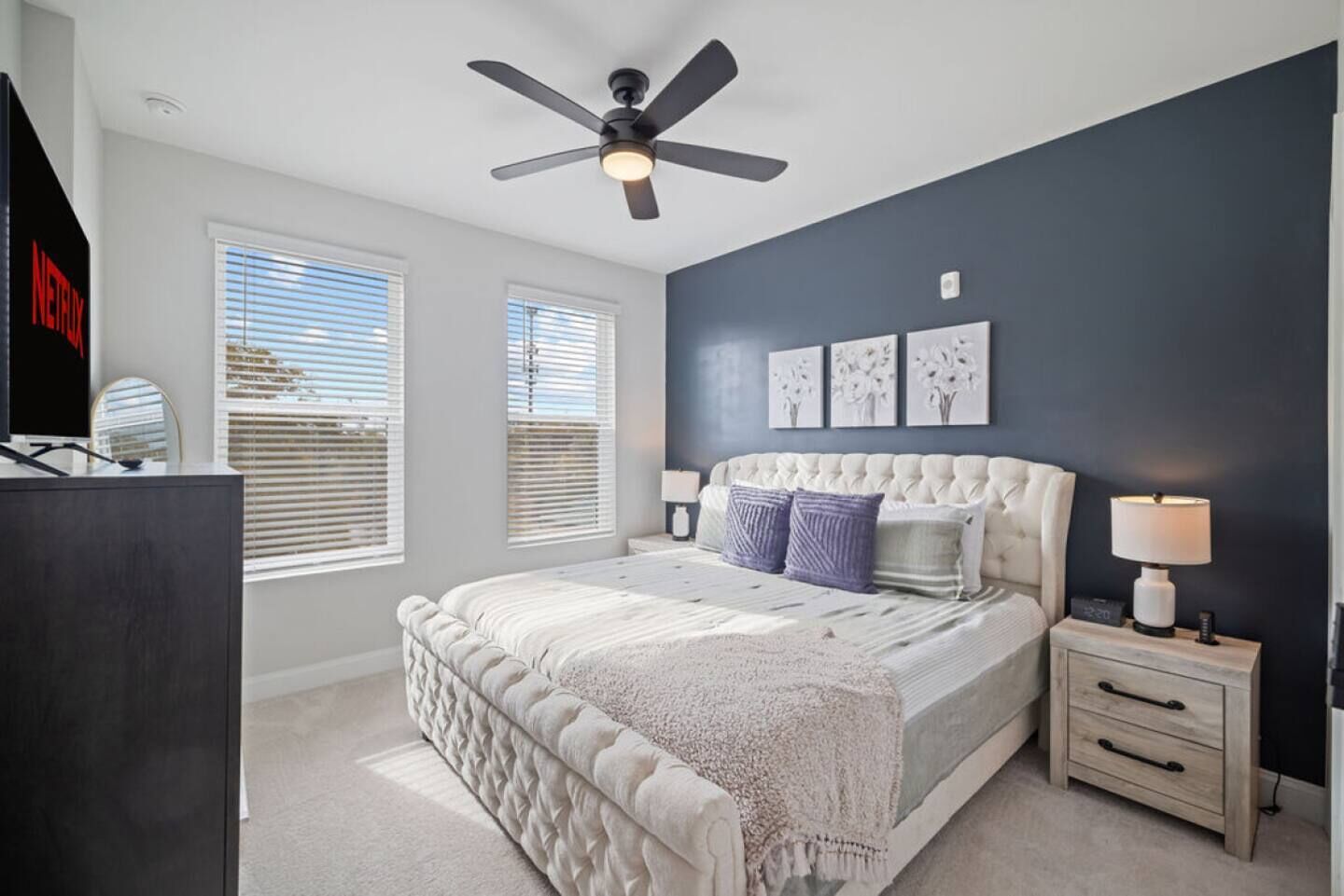 A bedroom with a bed, a nightstand, a lamp, a ceiling fan, and artwork on the wall.