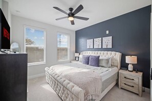 A bedroom with a bed, a nightstand, a lamp, a ceiling fan, and artwork on the wall. - Downtown Wake Forest Luxury Condo | Rooftop Terrace + EV Charger (Wake Forest)