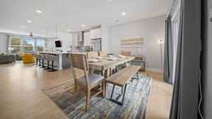 A modern kitchen with white cabinets, a wooden dining table, and a gray rug. - Downtown Wake Forest Luxury Condo | Rooftop Terrace + EV Charger (Wake Forest)