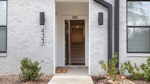 A modern building entrance with a number '200' above the door, a small porch area, and a brick facade. - Downtown Wake Forest Luxury Condo | Rooftop Terrace + EV Charger (Wake Forest)