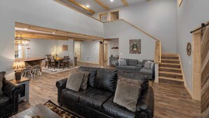 A spacious living area with a black leather sofa, wooden flooring, and a staircase leading to an upper level. - Boone Getaway | Dog Friendly, Hot Tub, Fire Pit! (Watauga County)