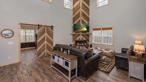 A spacious living room with a fireplace, wooden flooring, and large windows. - Boone Getaway | Dog Friendly, Hot Tub, Fire Pit! (Watauga County)