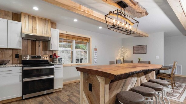 A modern kitchen with wooden cabinets, a large island with bar stools, and a built-in oven. - Boone Getaway | Dog Friendly, Hot Tub, Fire Pit! (Watauga County)