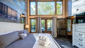 A bedroom with a large bed, a dresser, and a window with curtains. - Island in the Stream Spacious Creekside Cabin - Wi-Fi, Hot Tub, Arcade (Broken Bow)