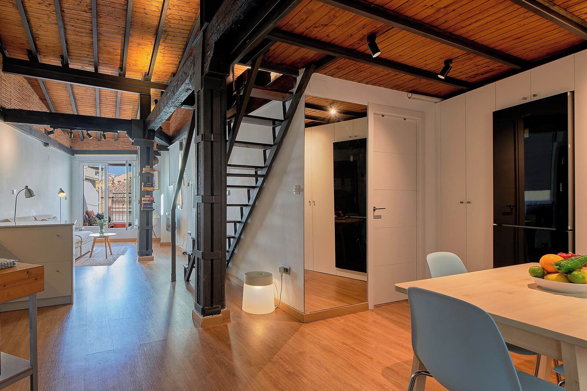 Un interior moderno con techo de madera, una escalera y un comedor con mesa y sillas.