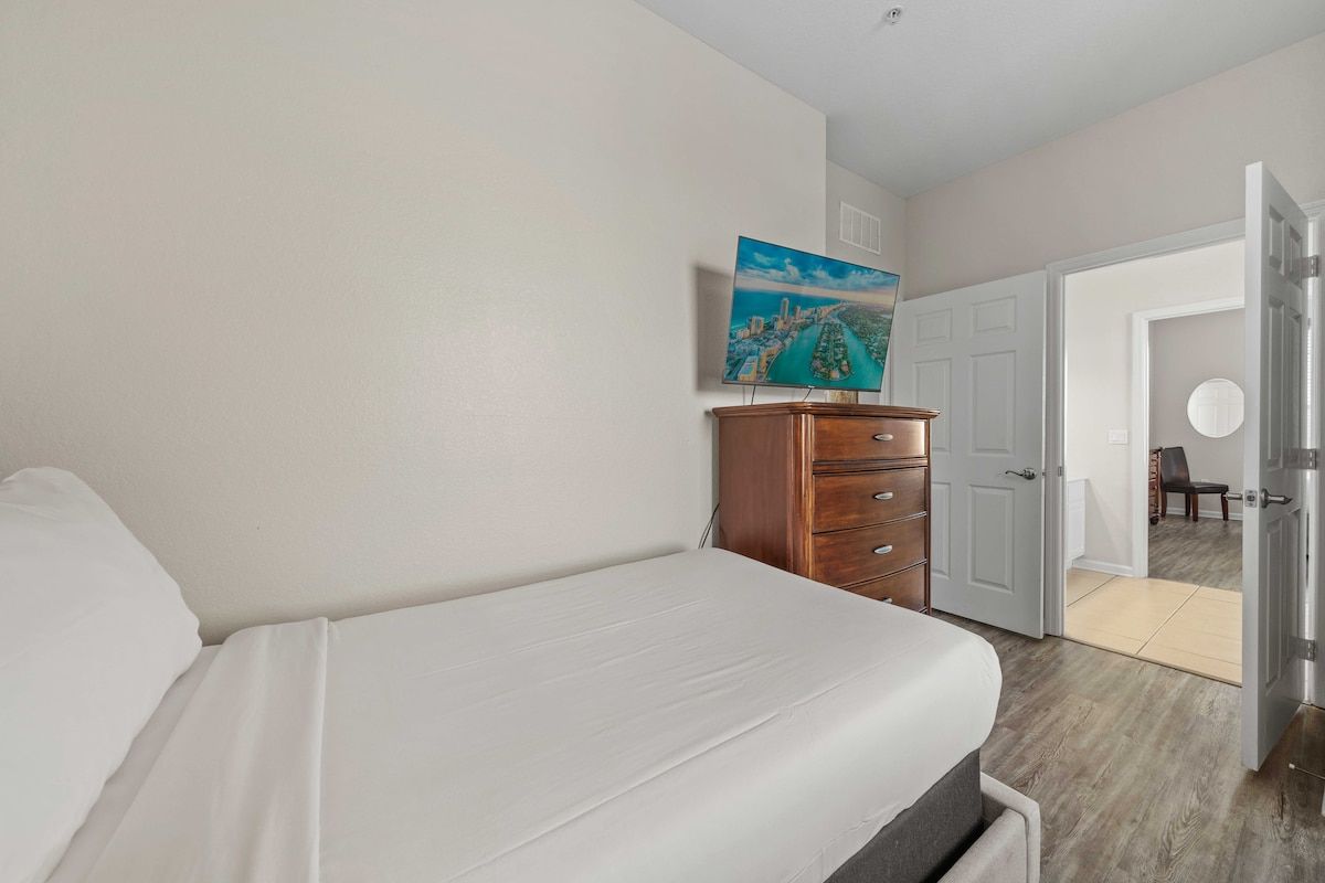A bedroom with a bed, a dresser, a door leading to another room, and a painting on the wall.
