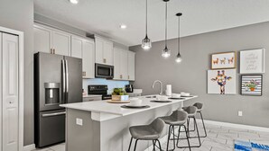 Une cuisine moderne dotée d’un îlot central, de tabourets de bar, d’appareils électroménagers en acier inoxydable et de luminaires suspendus.