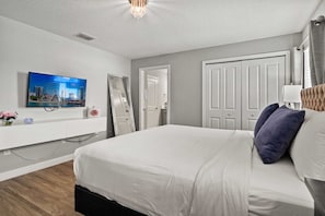 A bedroom with a bed, a television, a mirror, and a door.