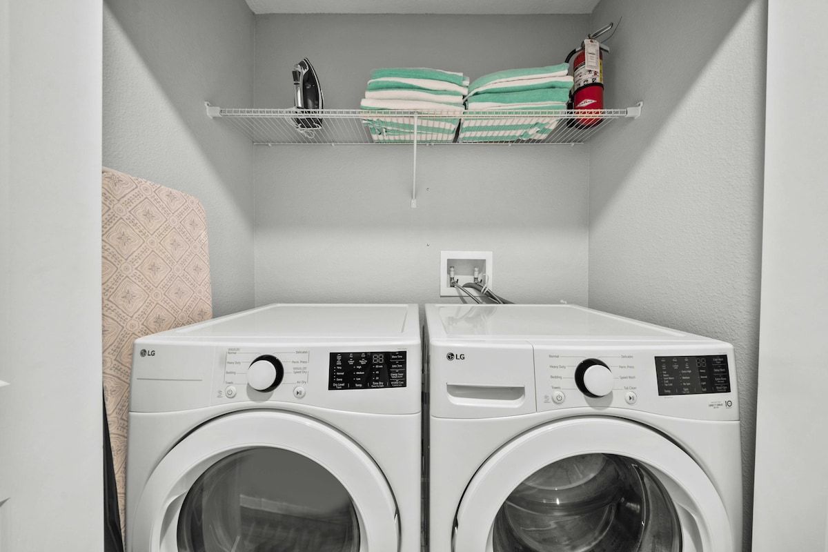 A laundry room with two white LG front-loading washing machines, a shelf with folded towels, and a fire extinguisher.